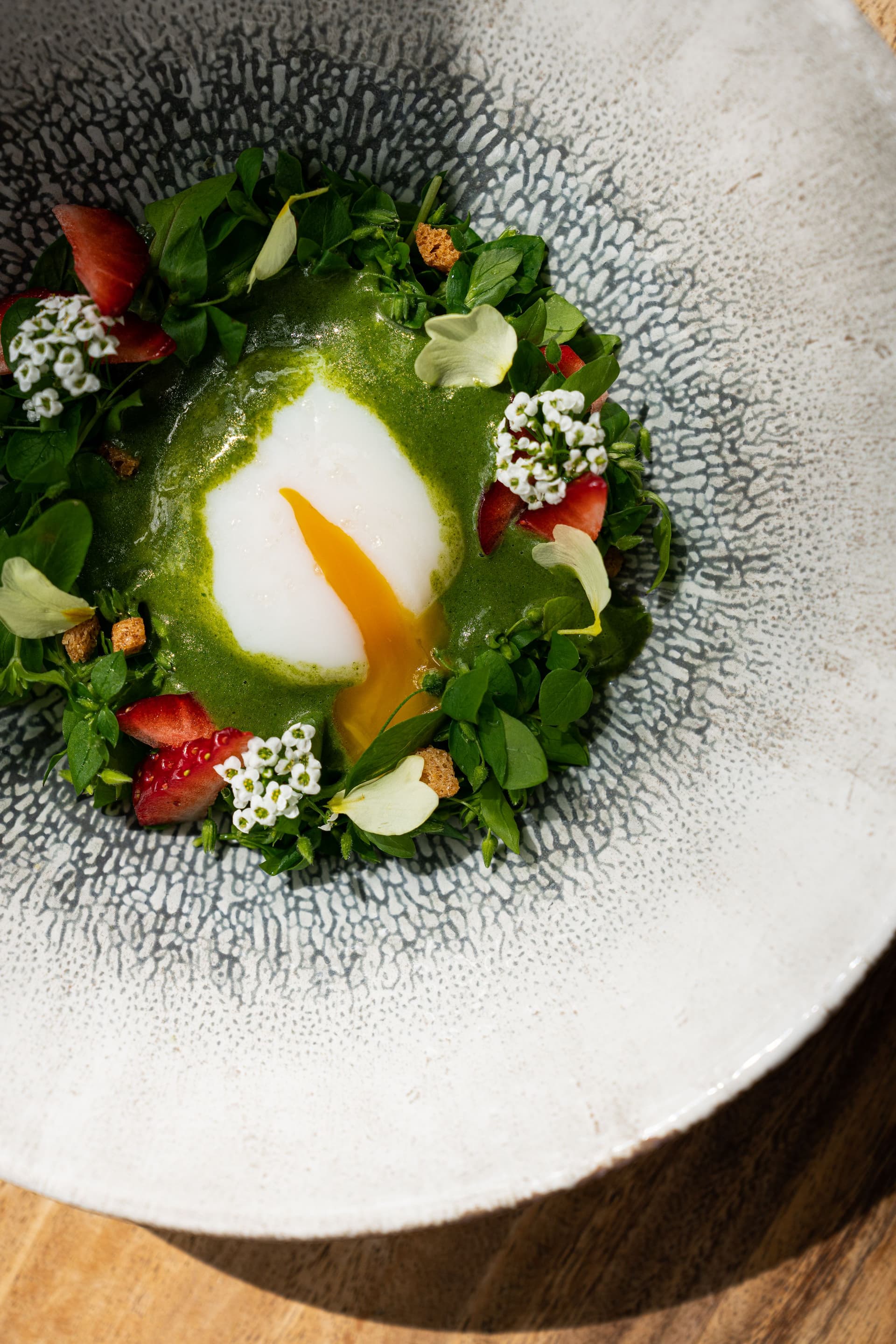Œuf poché avec sauce verte et fleurs comestibles.
